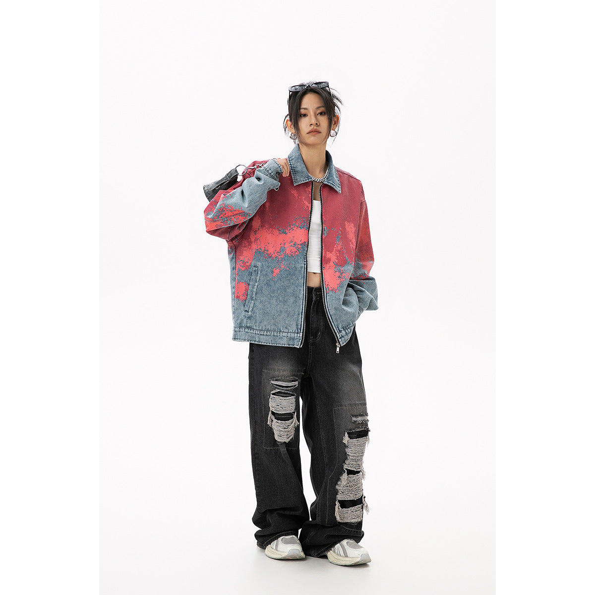 Model wearing an oversized blue denim zip jacket with coral-red mottled detailing, black ripped jeans and sneakers, front