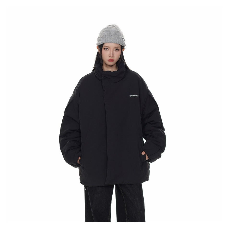 Front view of a model wearing a black oversized padded jacket with a high collar and small white chest lettering.