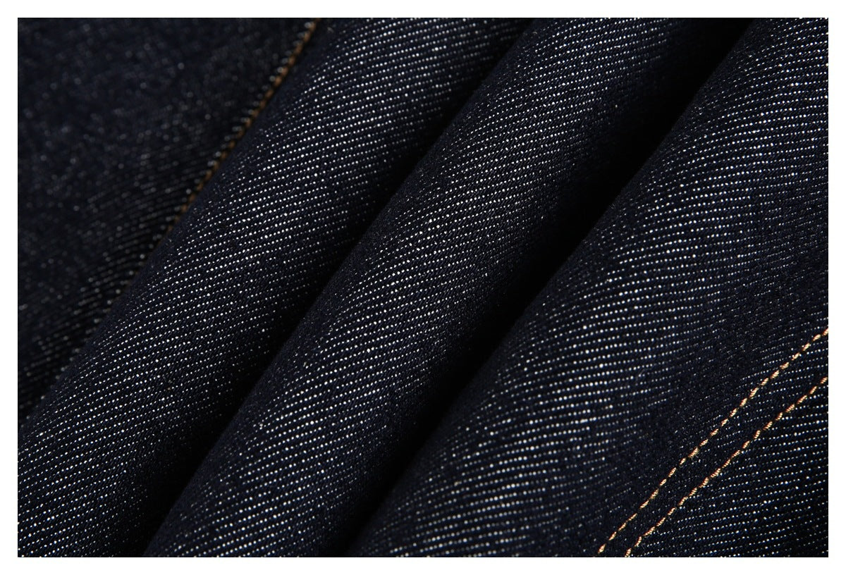 Close-up of dark indigo denim with visible diagonal weave and tan seam stitching.