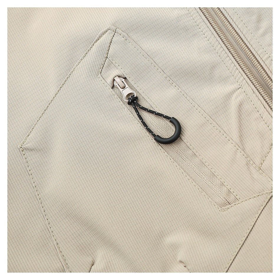 Close-up of a beige vest pocket with a diagonal zipper and black pull cord.