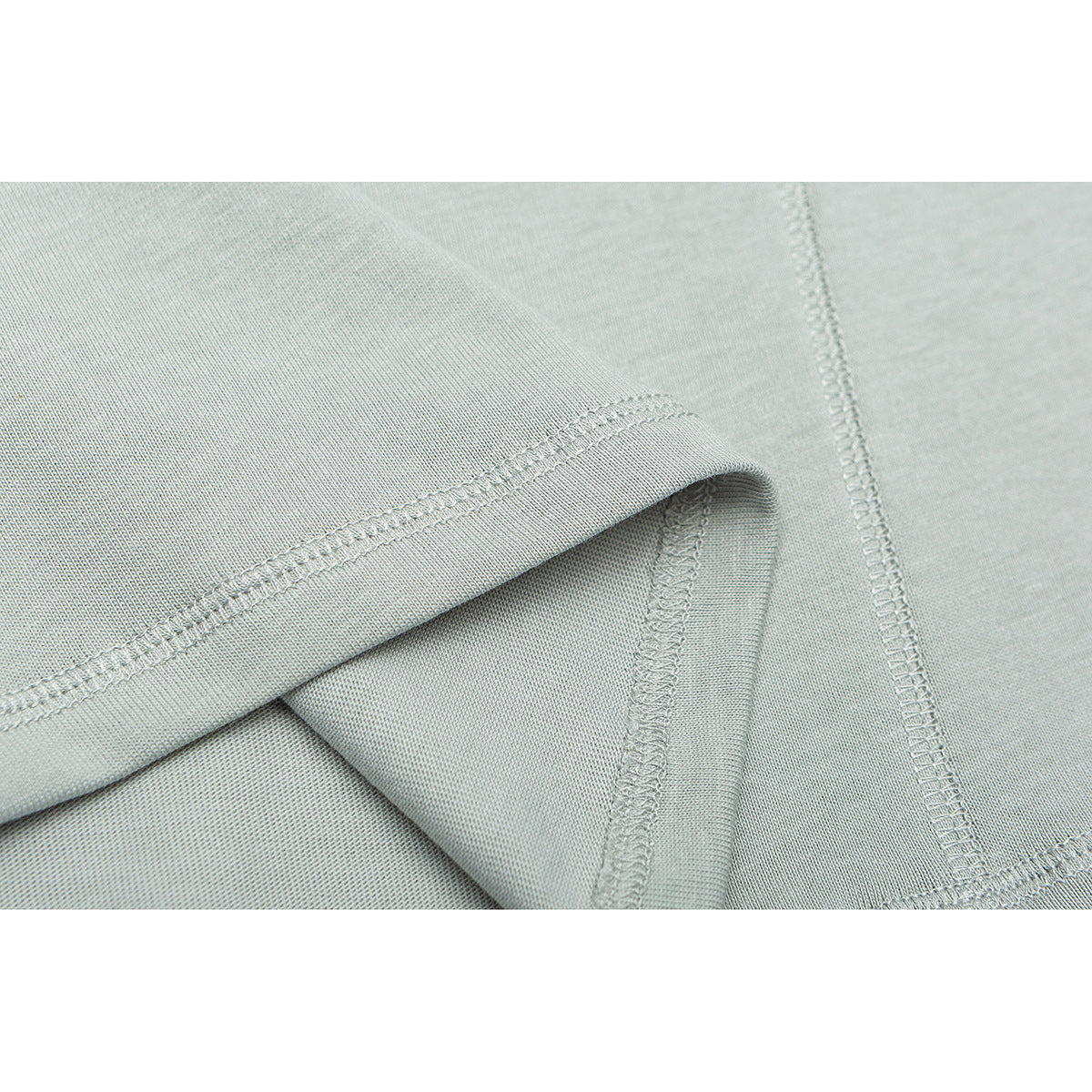 Close-up of pale sage shirt fabric showing a folded hem and stitching.