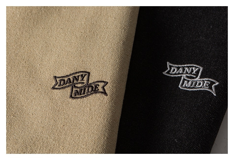 Close-up of embroidered lettering on beige and black textured garment fabric.