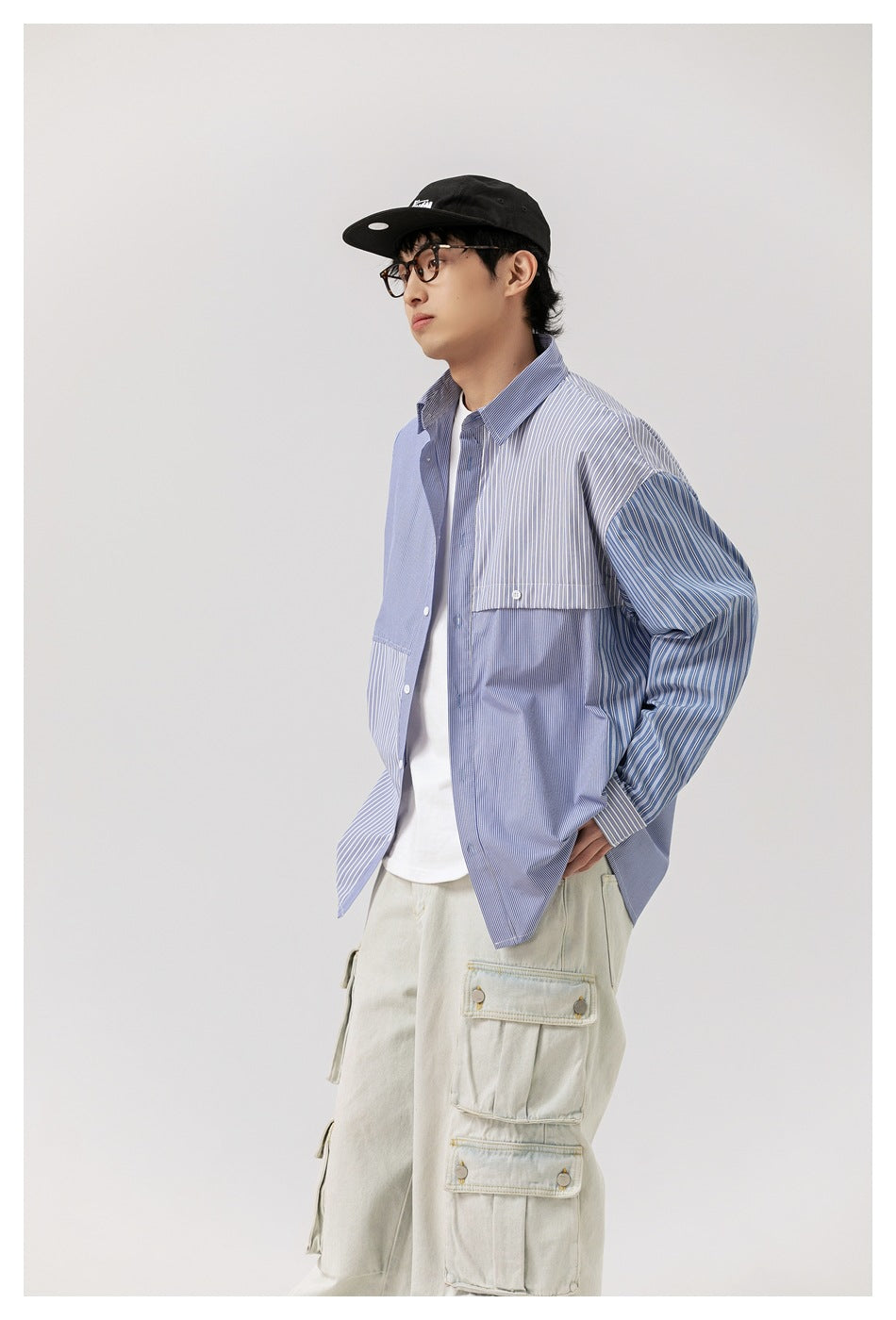 Three-quarter view of a model wearing a blue striped patchwork button-up shirt and pale cargo pants.