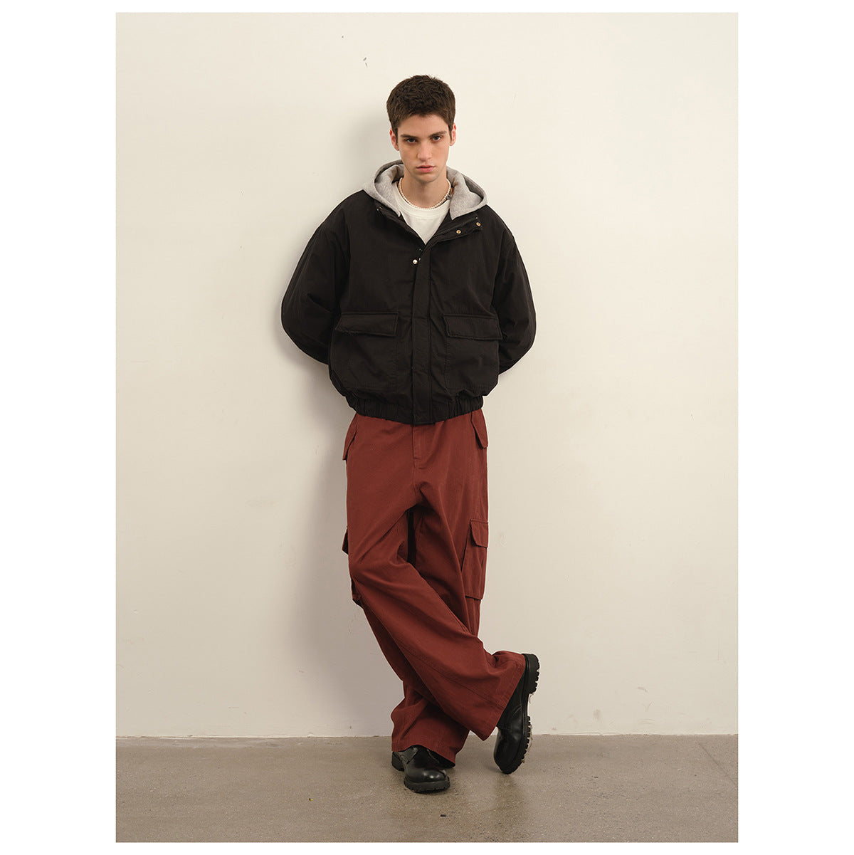 Model wearing a black hooded jacket with flap pockets, rust cargo pants, and black boots.