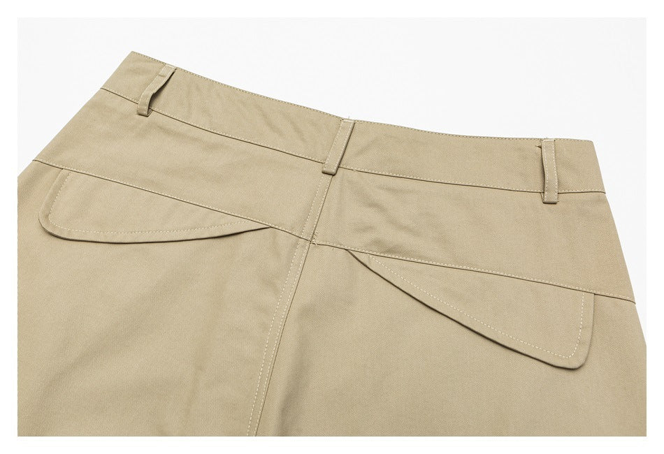 Close-up of beige trousers showing the waistband, belt loops, and overlapping curved front pocket panels.