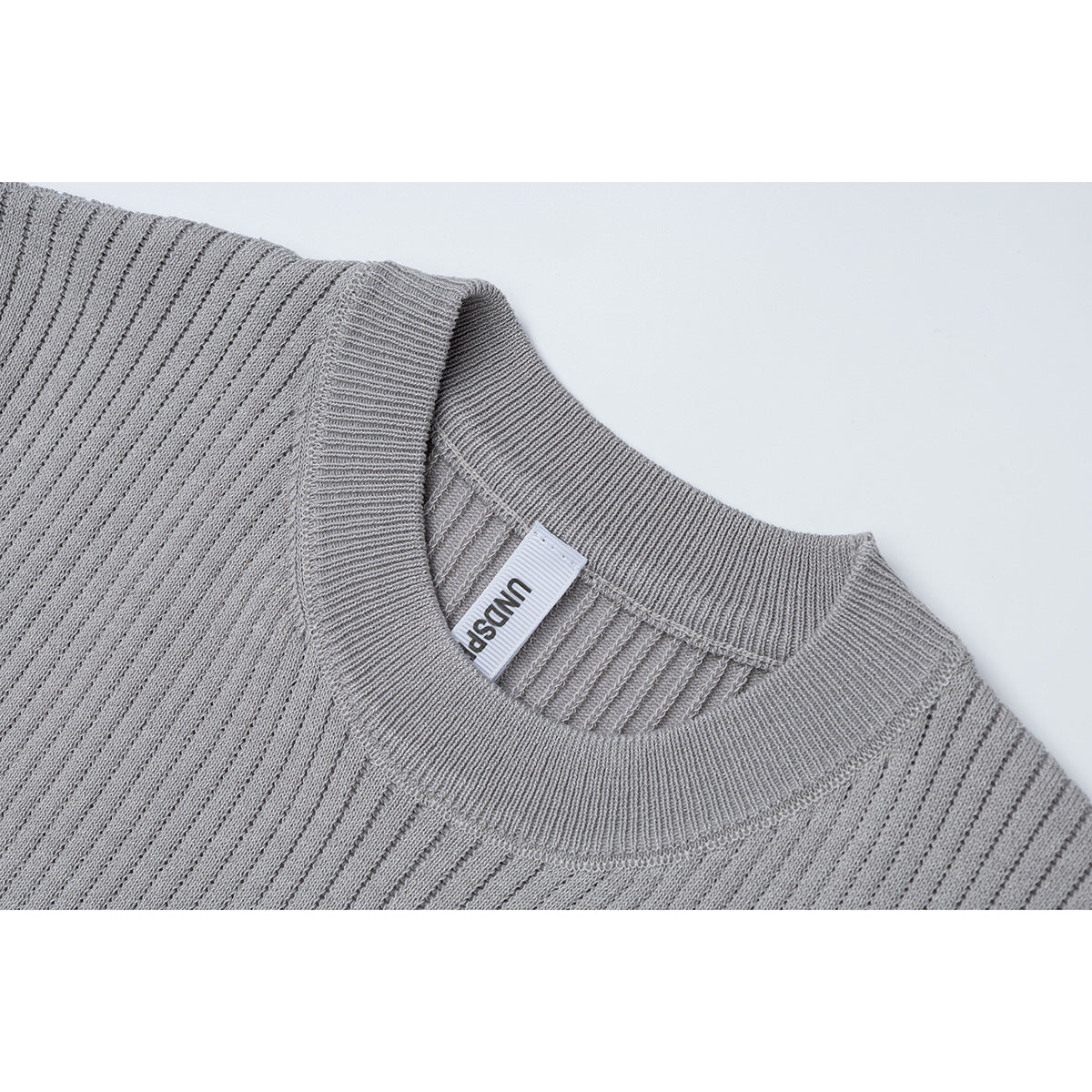 Close-up of a gray ribbed knit T-shirt's crew neckline and attached neck label.
