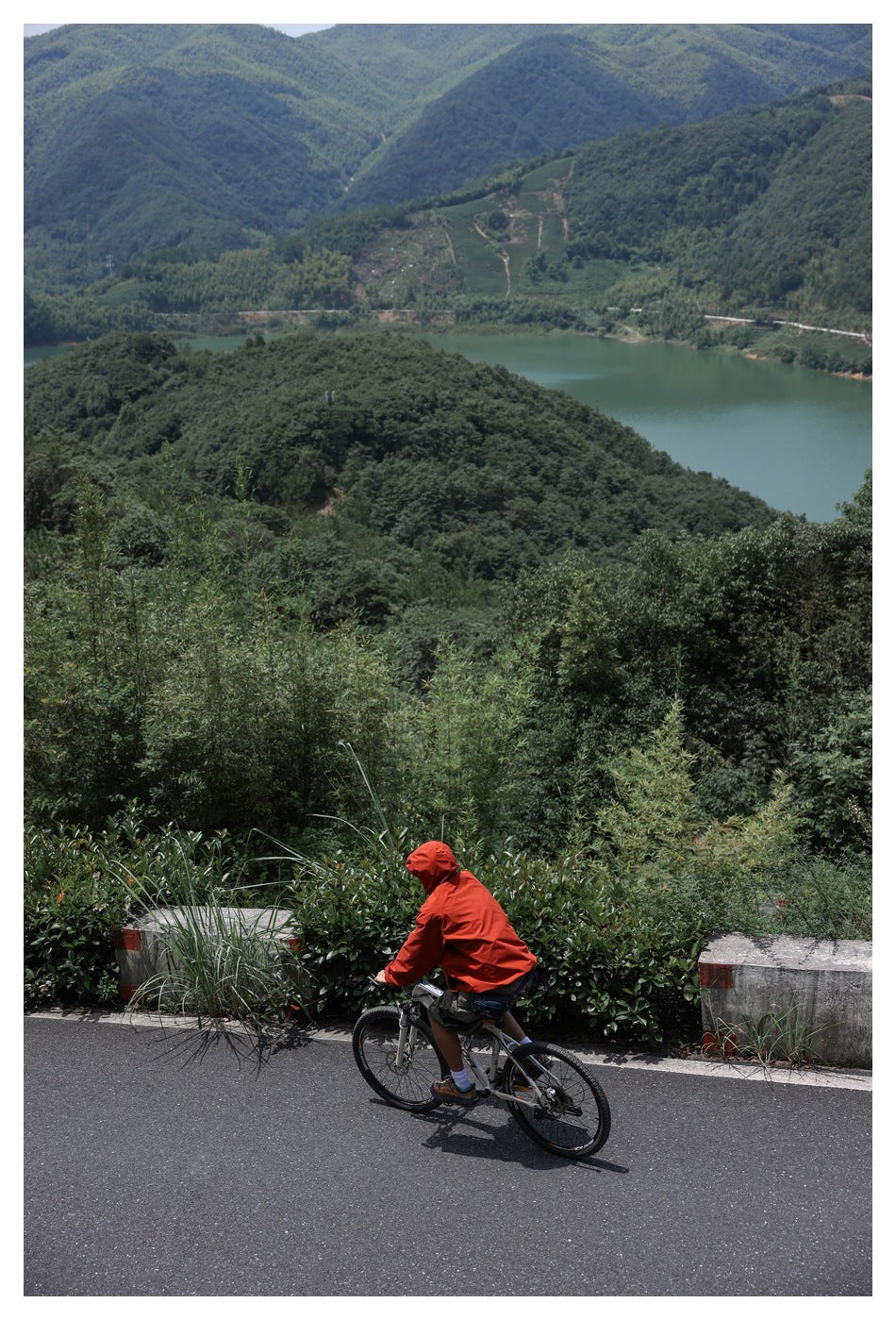 Distant view of a cyclist in a bright red hooded jacket riding along a mountain road.
