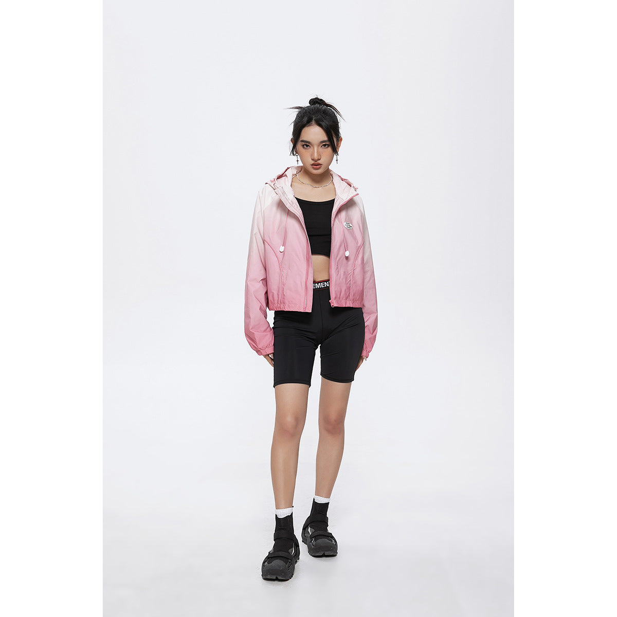 Model wearing a pink gradient hooded zip jacket with black cycling shorts, shown full length from the front.
