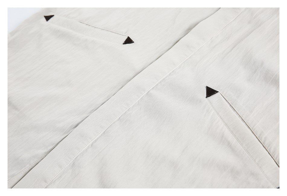 Close-up of two pocket openings and the placket on a light beige shirt, with dark triangular accents.