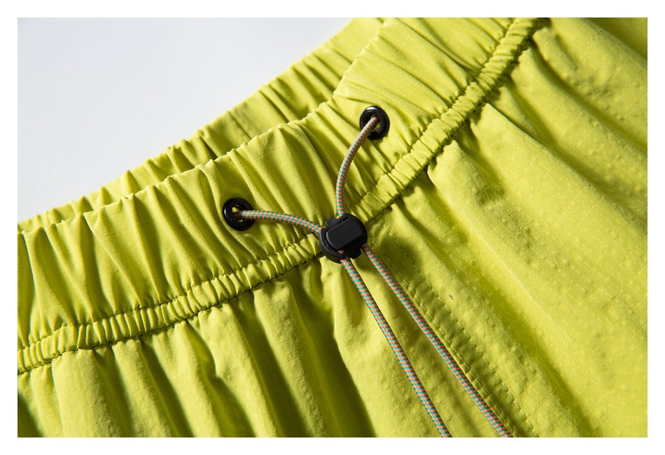 Close-up of lime-yellow shorts' gathered elastic waistband with a multicolored drawcord and black stopper.