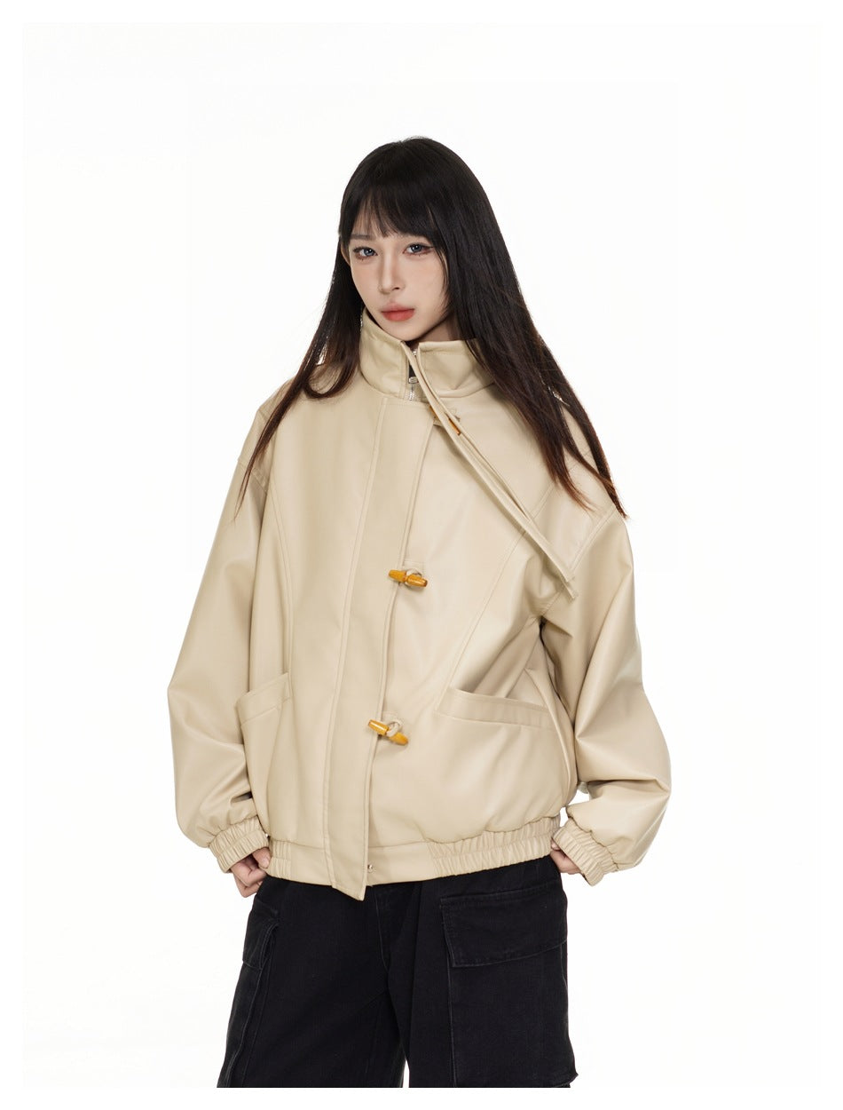 Model wearing a closed beige oversized jacket with a high collar, wooden toggles, elastic cuffs and hem, and large pockets.