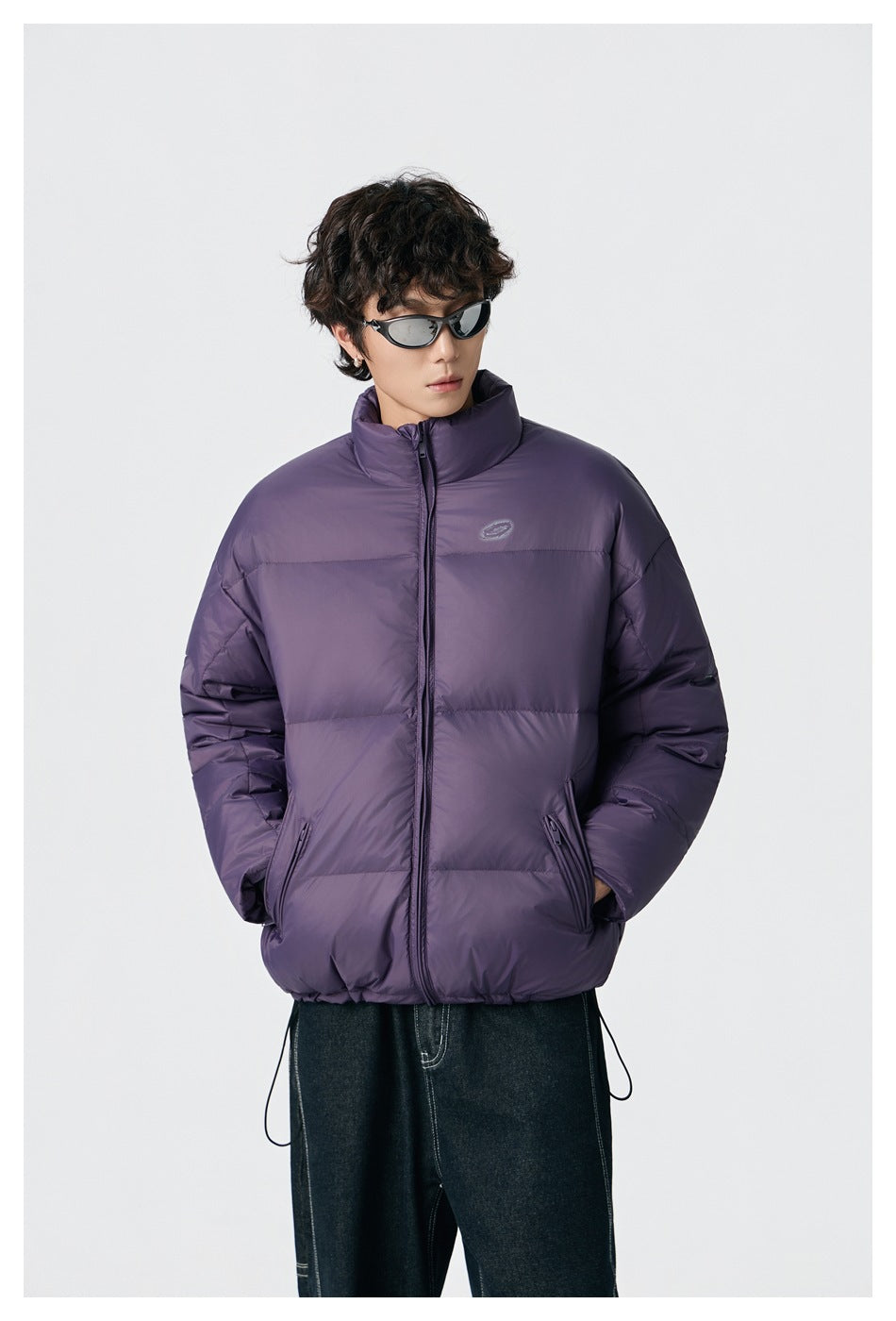 Model wearing a purple quilted puffer jacket with a high collar, front zipper and zip pockets.