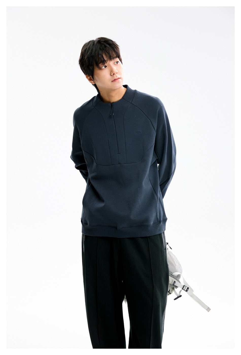 Model wearing a dark navy quarter-zip sweatshirt with curved panel seams and black wide-leg pants.