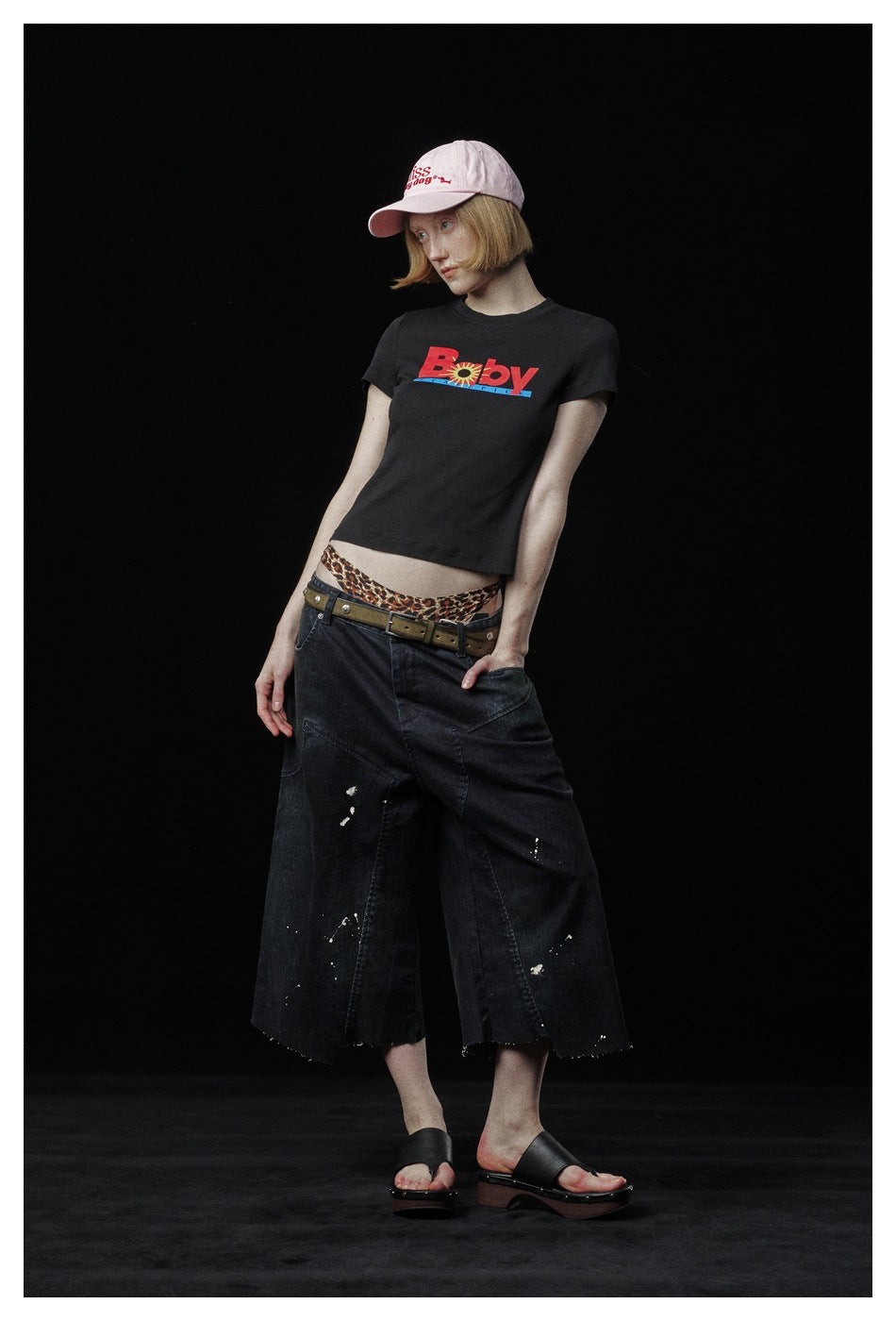 Model in a black graphic T-shirt and wide cropped black jeans, shown in a tilted full-length pose.