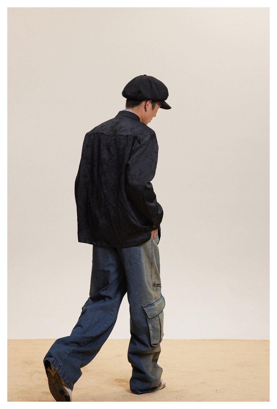 Rear view of a model wearing a black tonal-patterned jacket and loose blue cargo jeans.