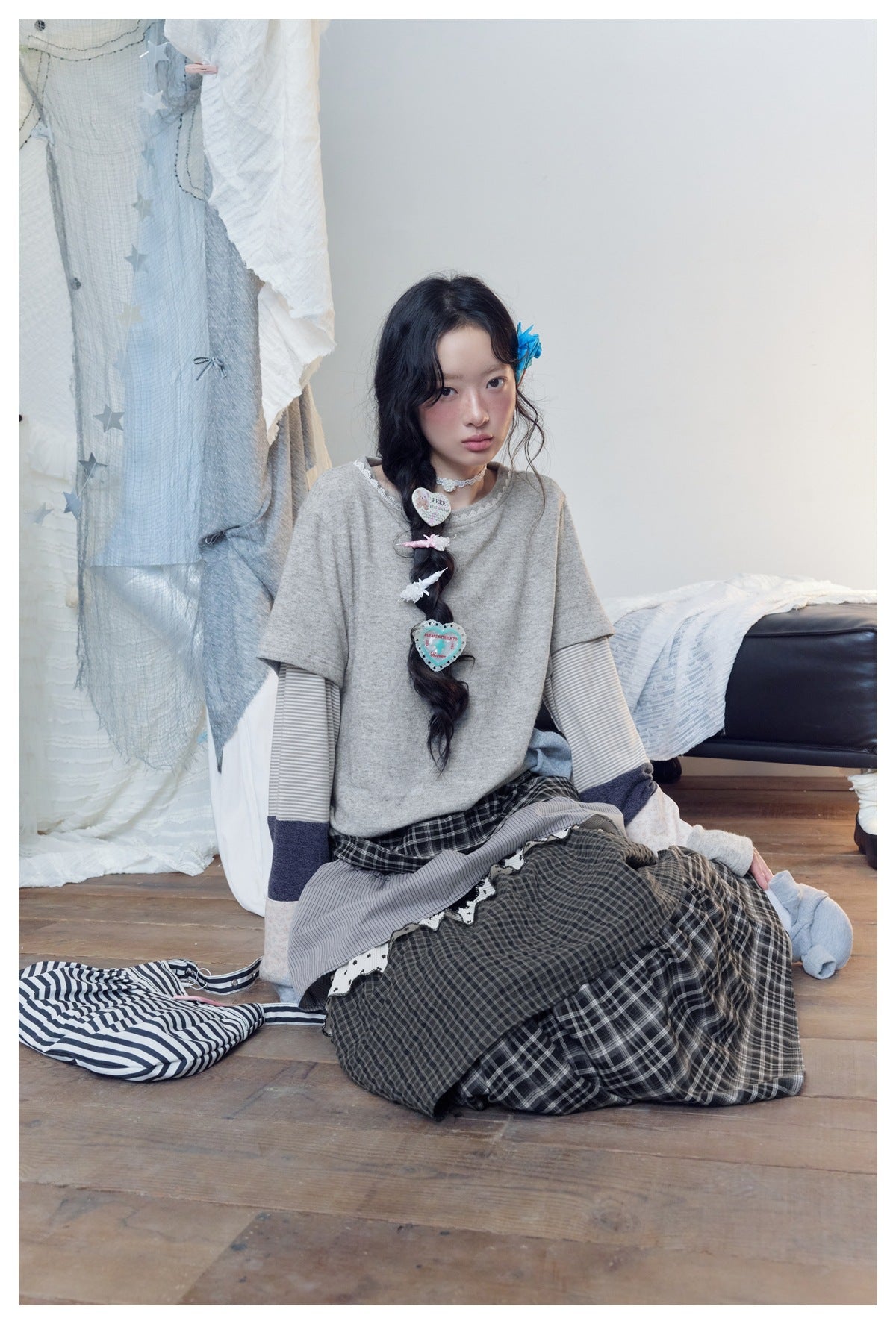Seated model wearing a gray patchwork-sleeve top and layered dark plaid skirt.