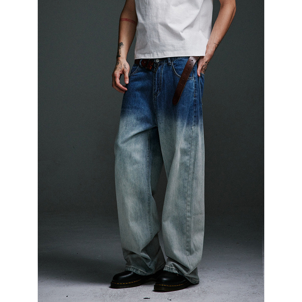 Cropped model wearing very wide blue jeans with a dark-to-pale wash, brown belt, white T-shirt and black shoes.