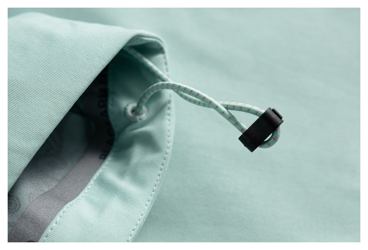 Close-up of a mint garment hood with a speckled drawcord threaded through an eyelet and a black toggle.