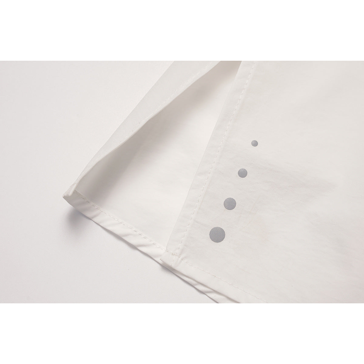 Close-up of a white skirt hem and seam with four gray dots of increasing size.