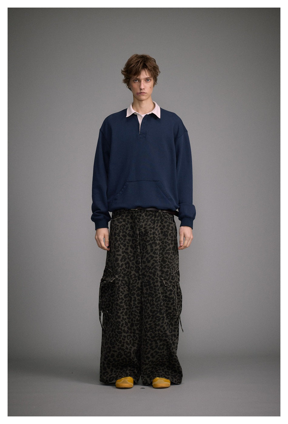 Model wearing navy polo-collar sweatshirt with cream collar and kangaroo pocket, styled with wide leopard-print pants