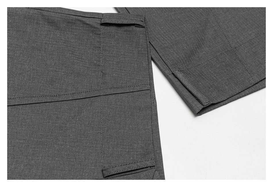 Close-up of dark gray trousers with stitched seams and small fabric tabs beside an overlapping leg section.