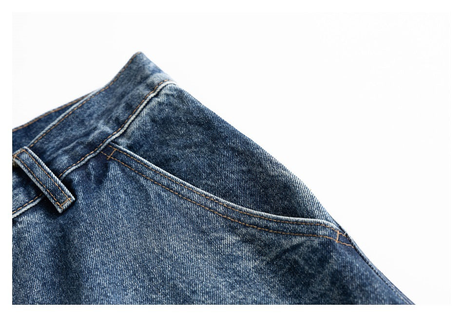 Close-up of blue washed jeans showing the waistband, belt loop and curved front pocket seam.