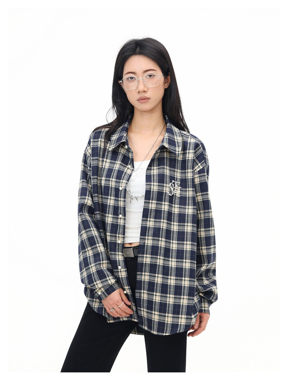 Close view of a model wearing an open navy and cream plaid shirt with a beaded chest embellishment over a white top.