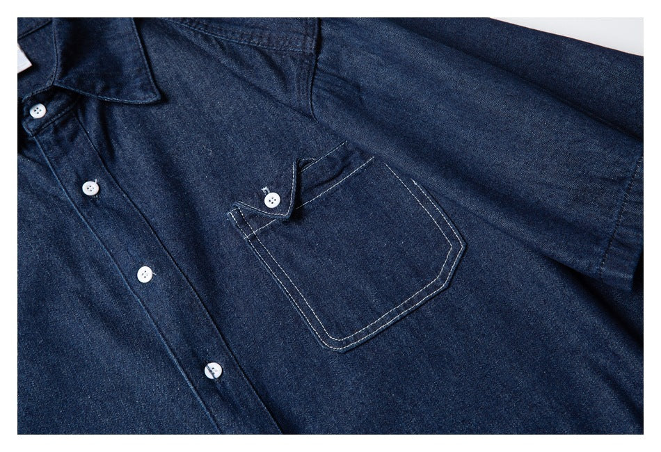 Close-up of a dark indigo shirt front with white buttons and a stitched chest pocket with a buttoned flap.
