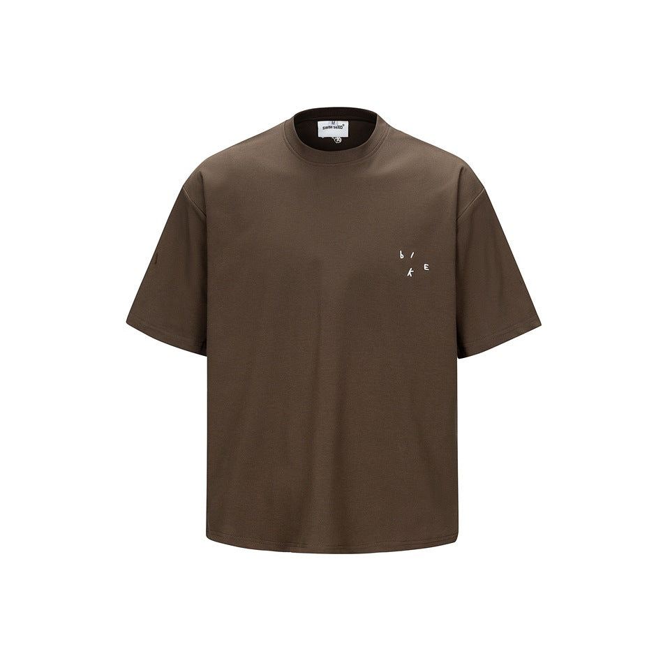 Brown short-sleeve crew-neck T-shirt, front view, with small white scattered-letter mark on left chest