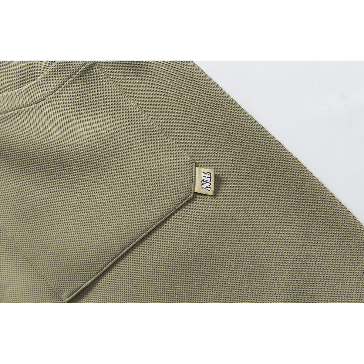 Close-up of olive textured fabric with a small sewn NB label.