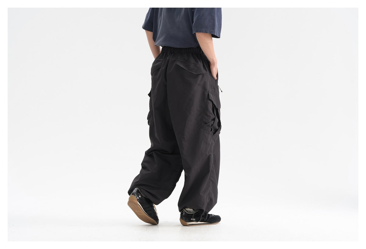 Rear view of a model wearing loose black cargo pants with an elastic waist and flap pockets.