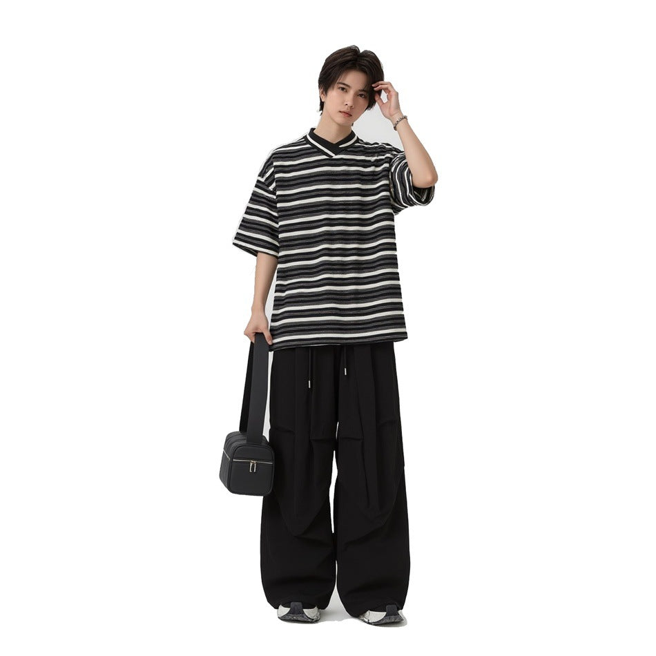 Model wearing the black and white striped T-shirt with black wide-leg pants and holding a small black bag