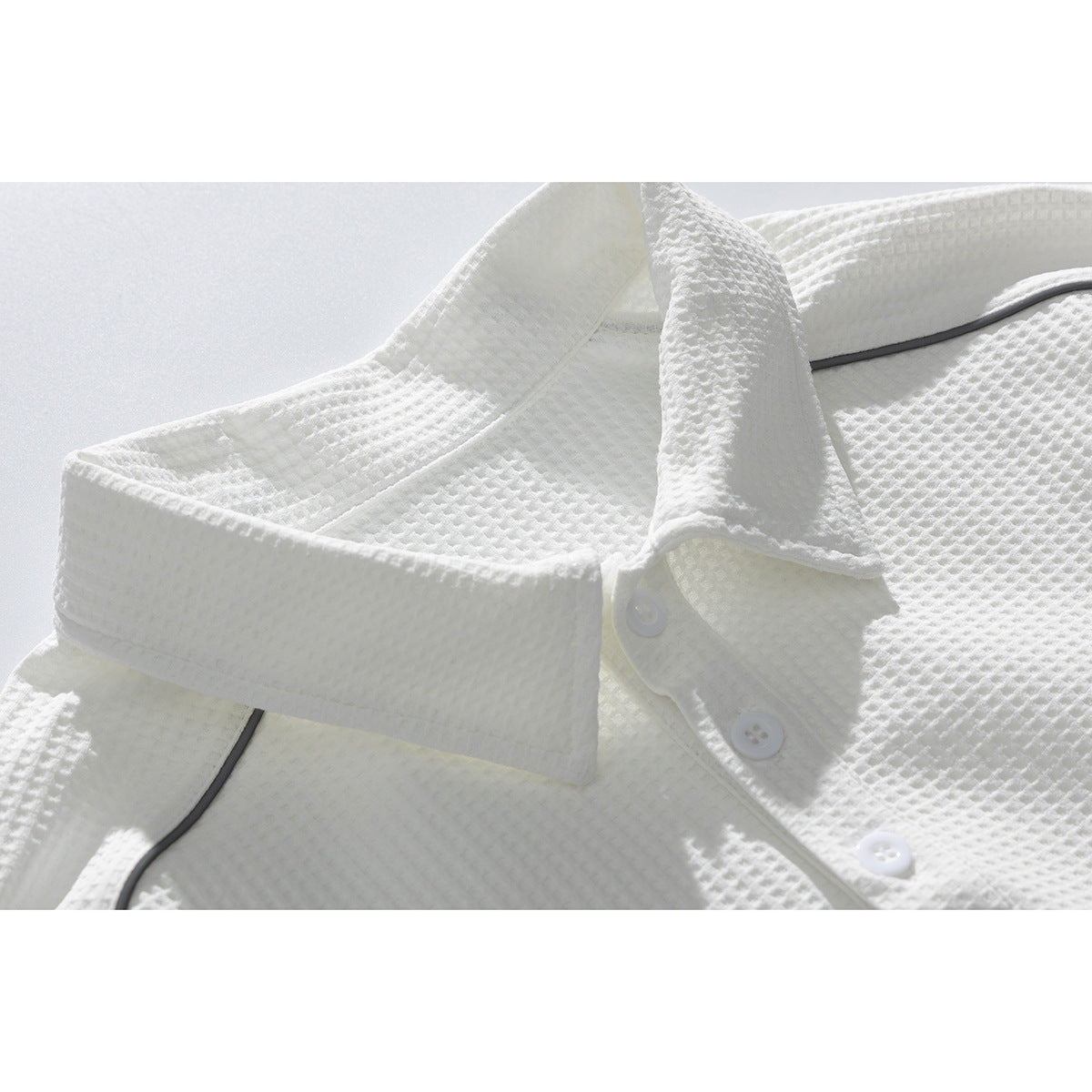 Close-up of a white textured polo shirt collar, three-button placket, and dark piping.