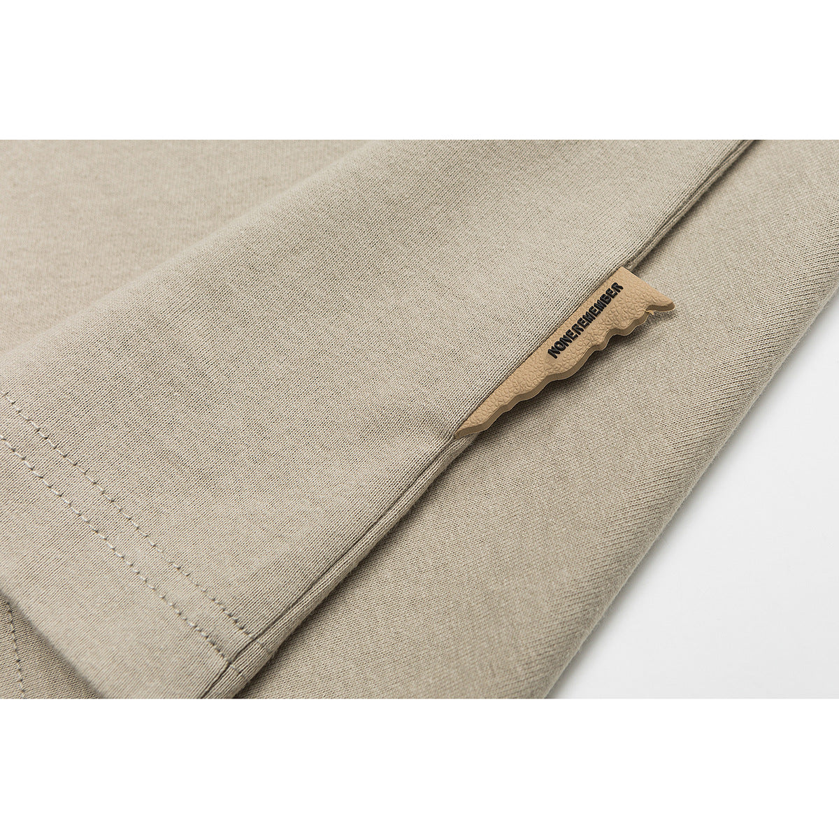 Close-up of a beige shirt's stitched side seam and small tan fabric label with black lettering.