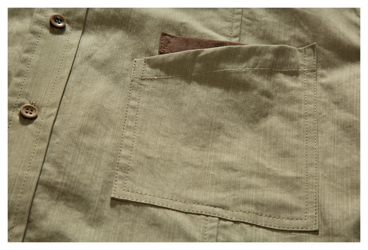 Close-up of an olive shirt's stitched chest pocket with a brown fabric accent peeking above it.