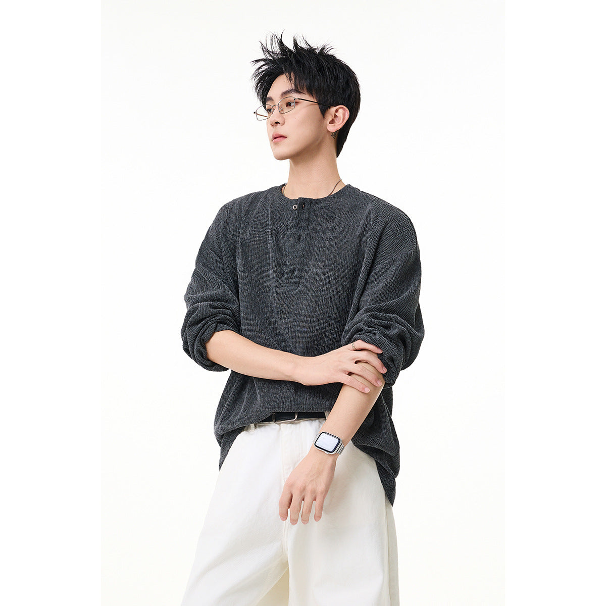 Model wearing a charcoal gray textured long-sleeve henley with a short button placket and white trousers, front view.
