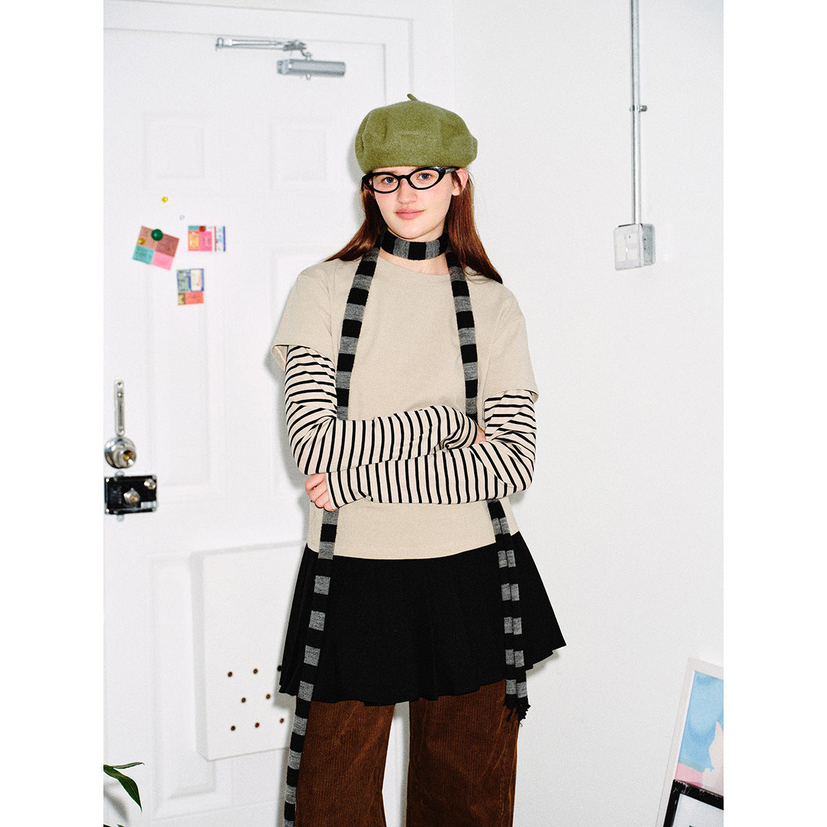 Front view of a model wearing a beige short-sleeve top over black-striped sleeves, a black skirt, brown trousers and striped