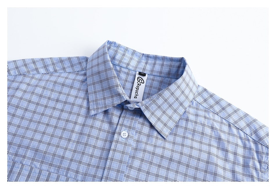 Close-up of a light blue plaid shirt collar and upper front with a visible inner neck label and white button.