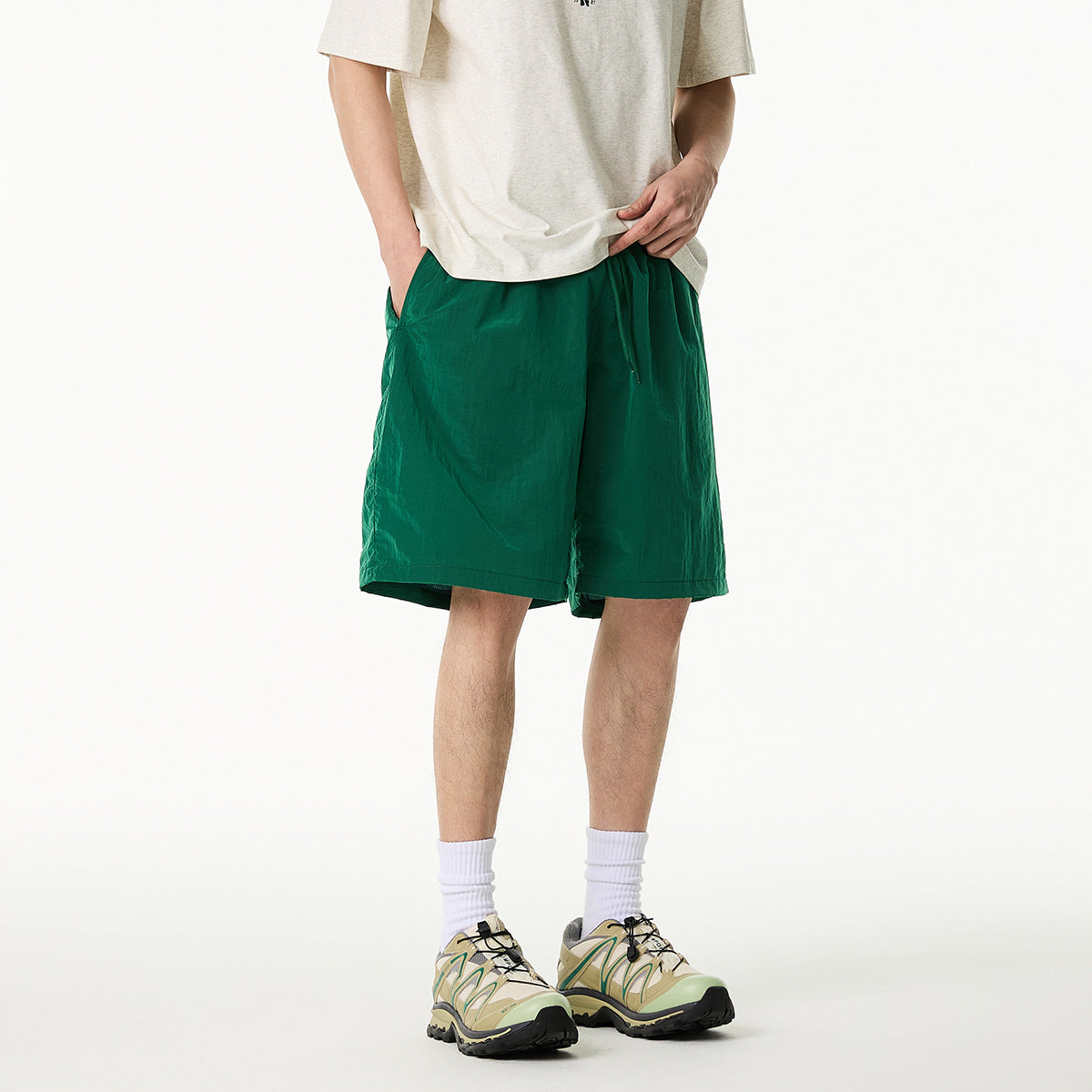 Cropped model wearing emerald green drawstring shorts with side pockets, a light T-shirt, white socks and trail shoes.