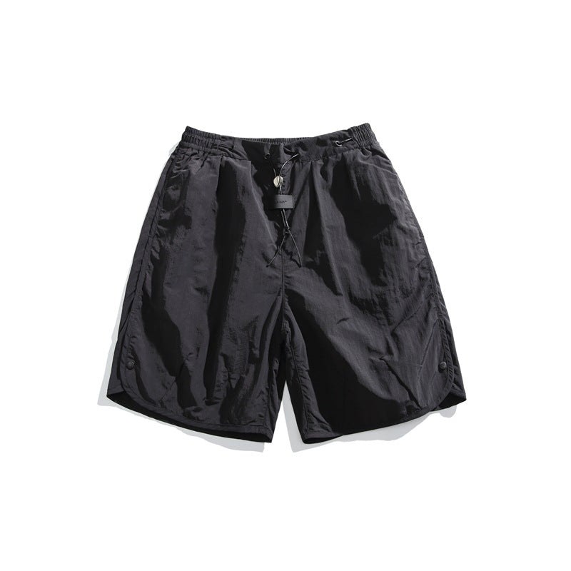 Black knee-length nylon-look shorts with elastic drawcord waist and curved snap-button side hems, flat lay