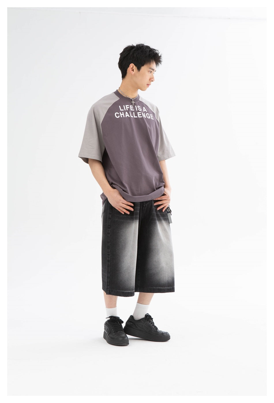 Model wearing black faded denim knee-length shorts with a gray and purple raglan tee, white socks and black sneakers