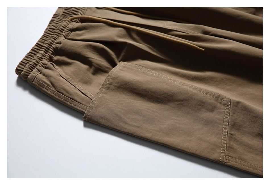 Close-up of brown pants showing an elastic waistband, drawstring, angled pocket opening and large leg patch pocket.