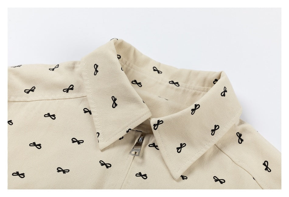 Closer view of the jacket's pointed collar and silver zipper against cream fabric patterned with black bows.