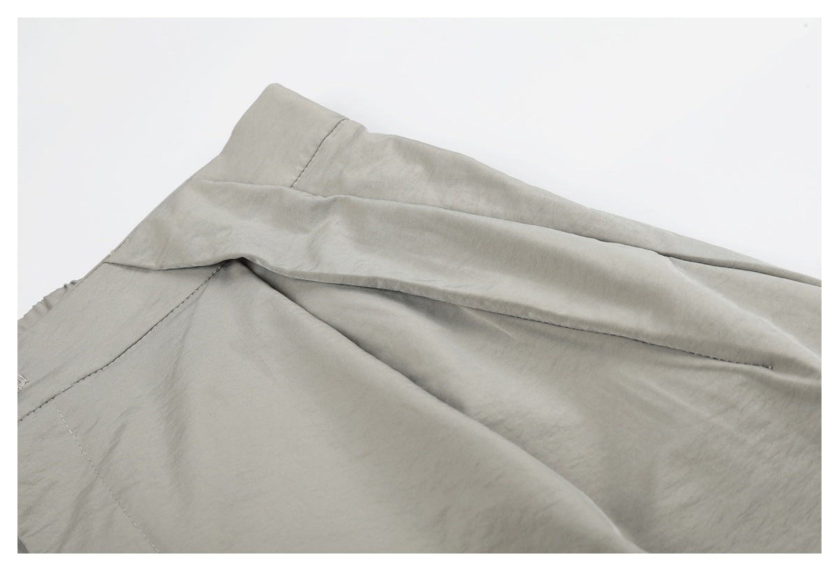 Close-up of light gray-beige trousers showing a seam and folded fabric.