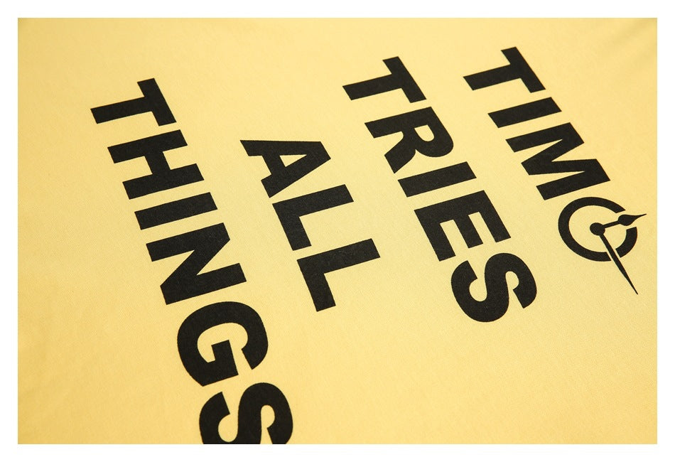 Close-up of black lettering and a clock-style graphic printed on yellow shirt fabric.
