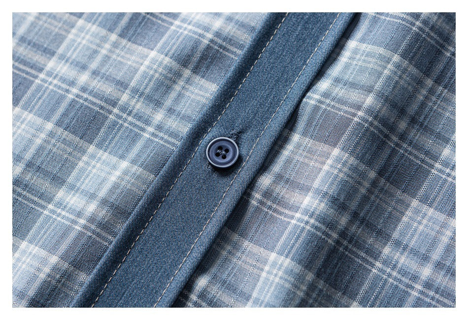 Close-up of a dark button on the denim placket of a gray-blue plaid shirt.