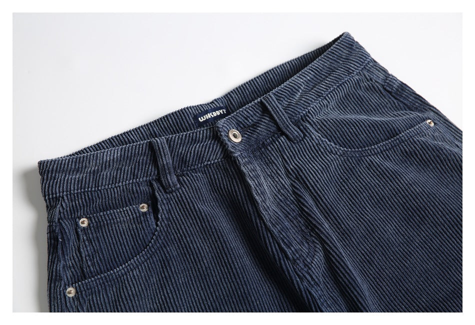 Close-up of the front waistband, button, belt loops and curved pockets on navy ribbed trousers.