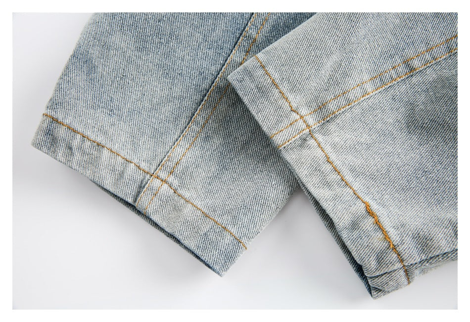 Close-up of folded denim hems with orange stitching and overlapping light-blue denim panels.