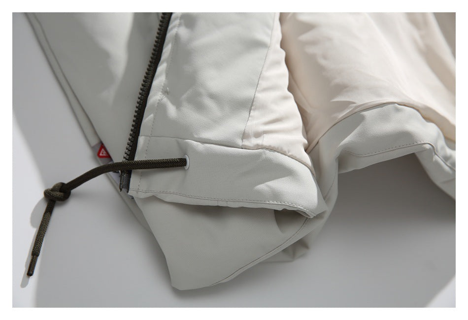 Close-up of a white jacket with a black zipper and dark drawcord threaded through an eyelet.