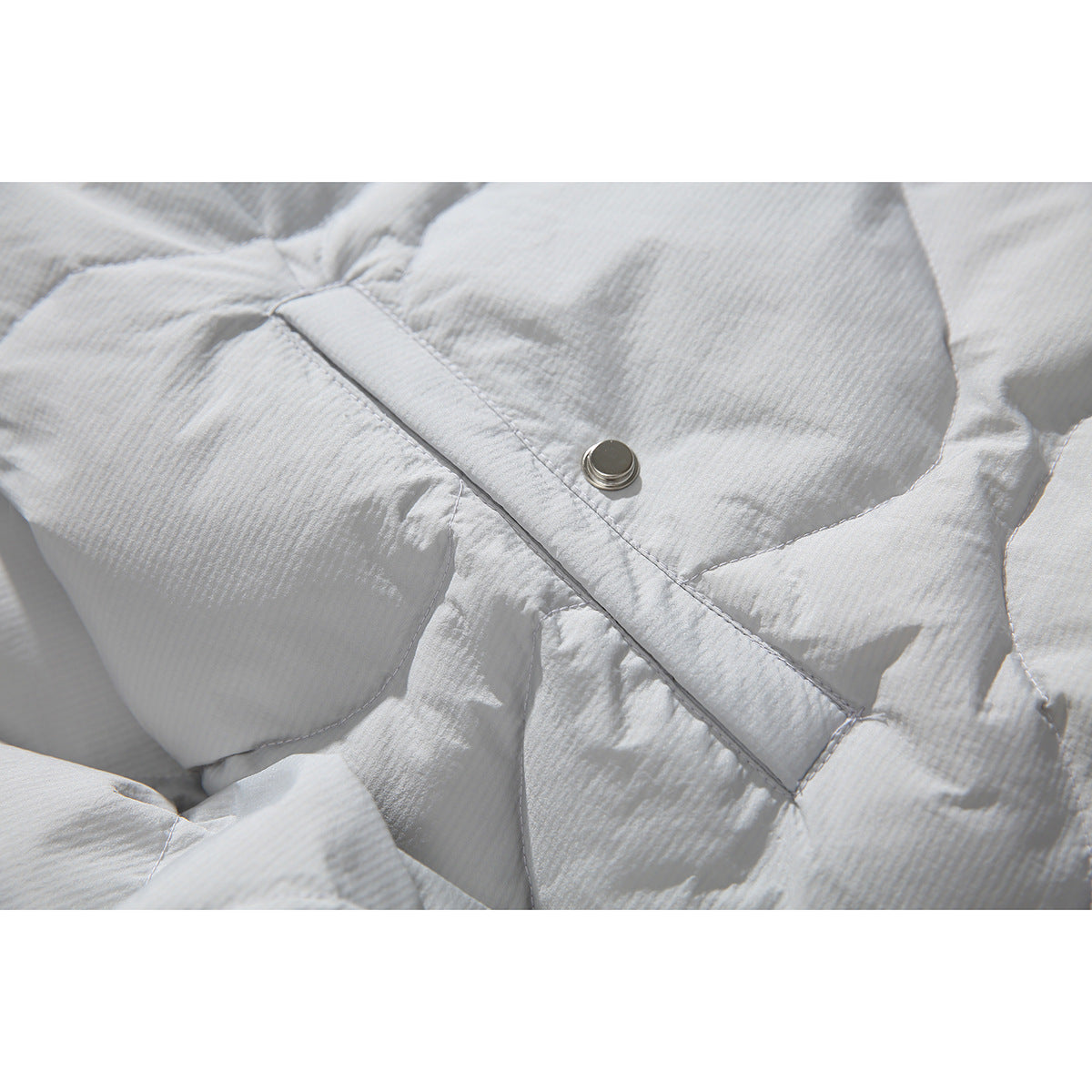 Close-up of a silver snap fastener and stitched placket on pale gray quilted jacket fabric.